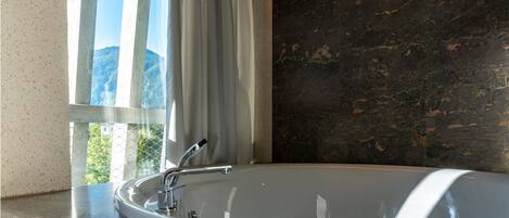 Un baño moderno con una bañera independiente, una ventana con cortinas y una pared de mármol oscuro.