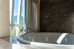 A modern bathroom with a freestanding bathtub, a window with curtains, and a dark marble wall.