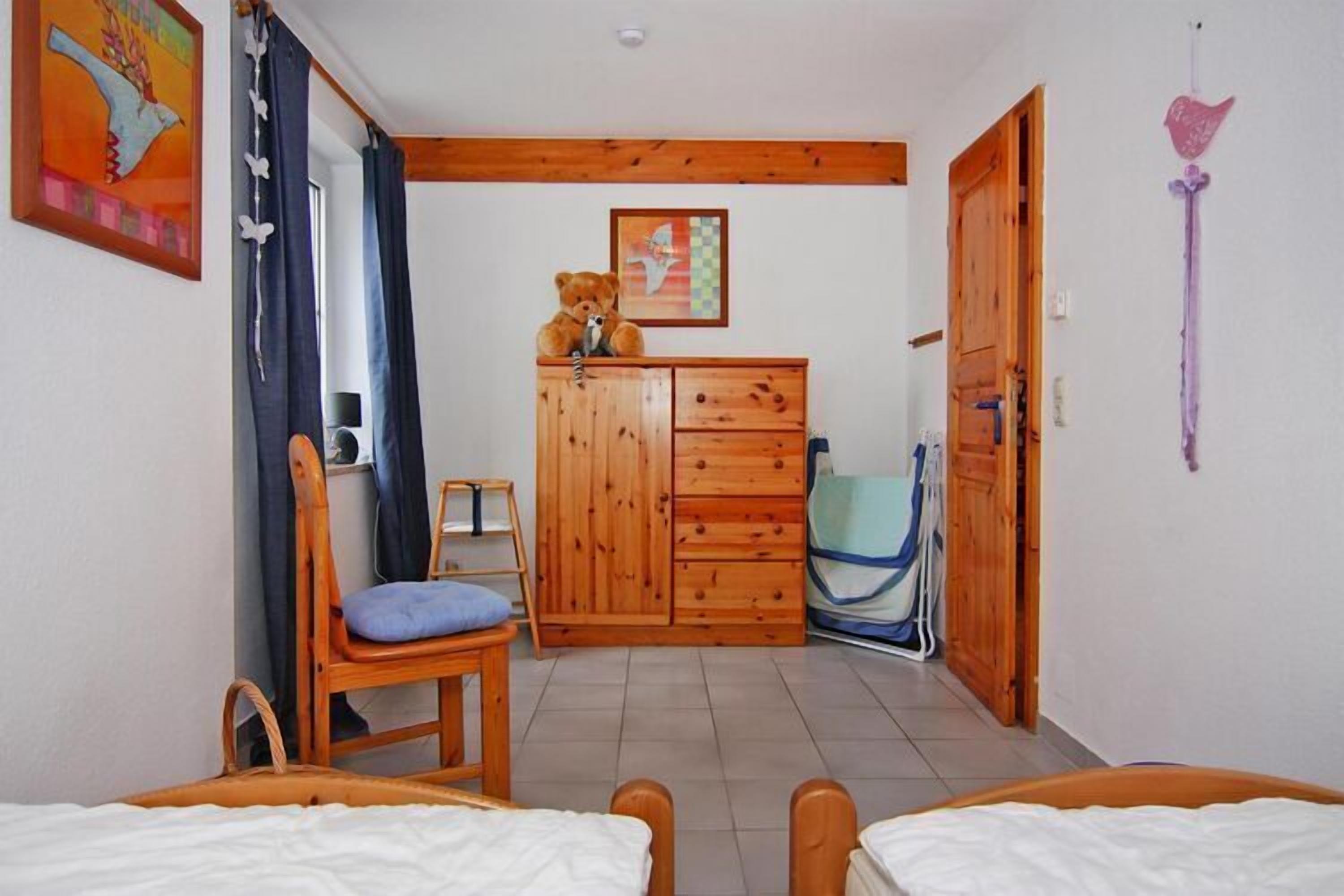 Quarto com duas camas, guarda-roupa de madeira, uma cadeira e uma mesinha.