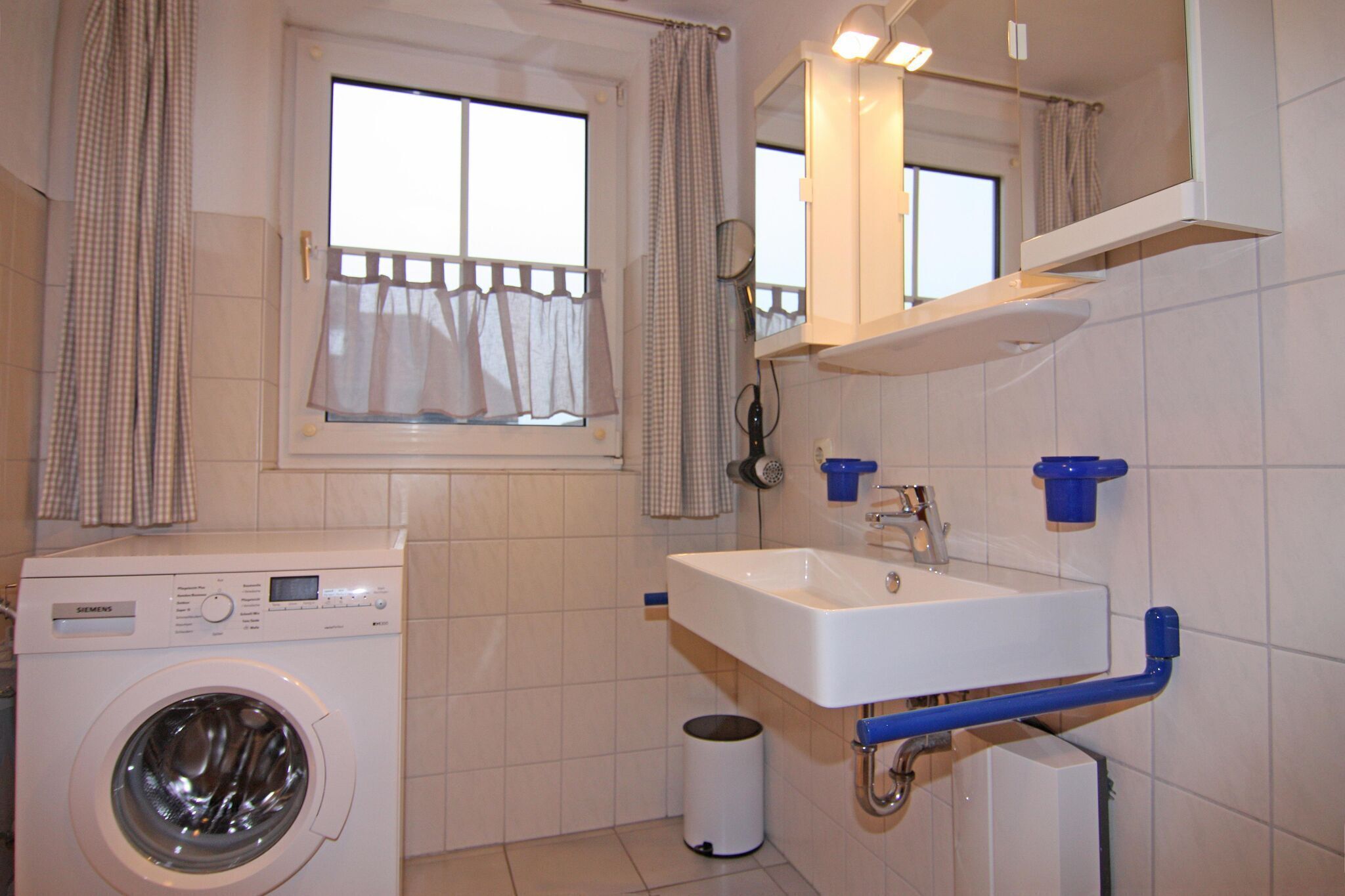 A compact bathroom with a washing machine, a sink, and a mirror.