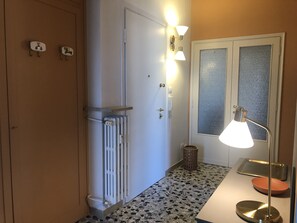 A hallway with a radiator, a wall-mounted light fixture, a trash bin, and a door with frosted glass panels. - Attic "Space to Light" (Verona)