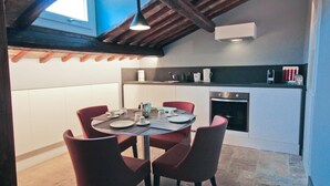 A compact kitchen with a dining area, featuring a modern stove, white cabinets, and a dining table with red chairs. - Two Bedroom Apartment (ROMA)
