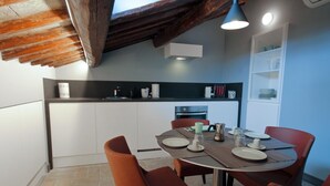 A modern kitchen with white cabinets, a dining table set for four, and a built-in oven. - Two Bedroom Apartment (ROMA)