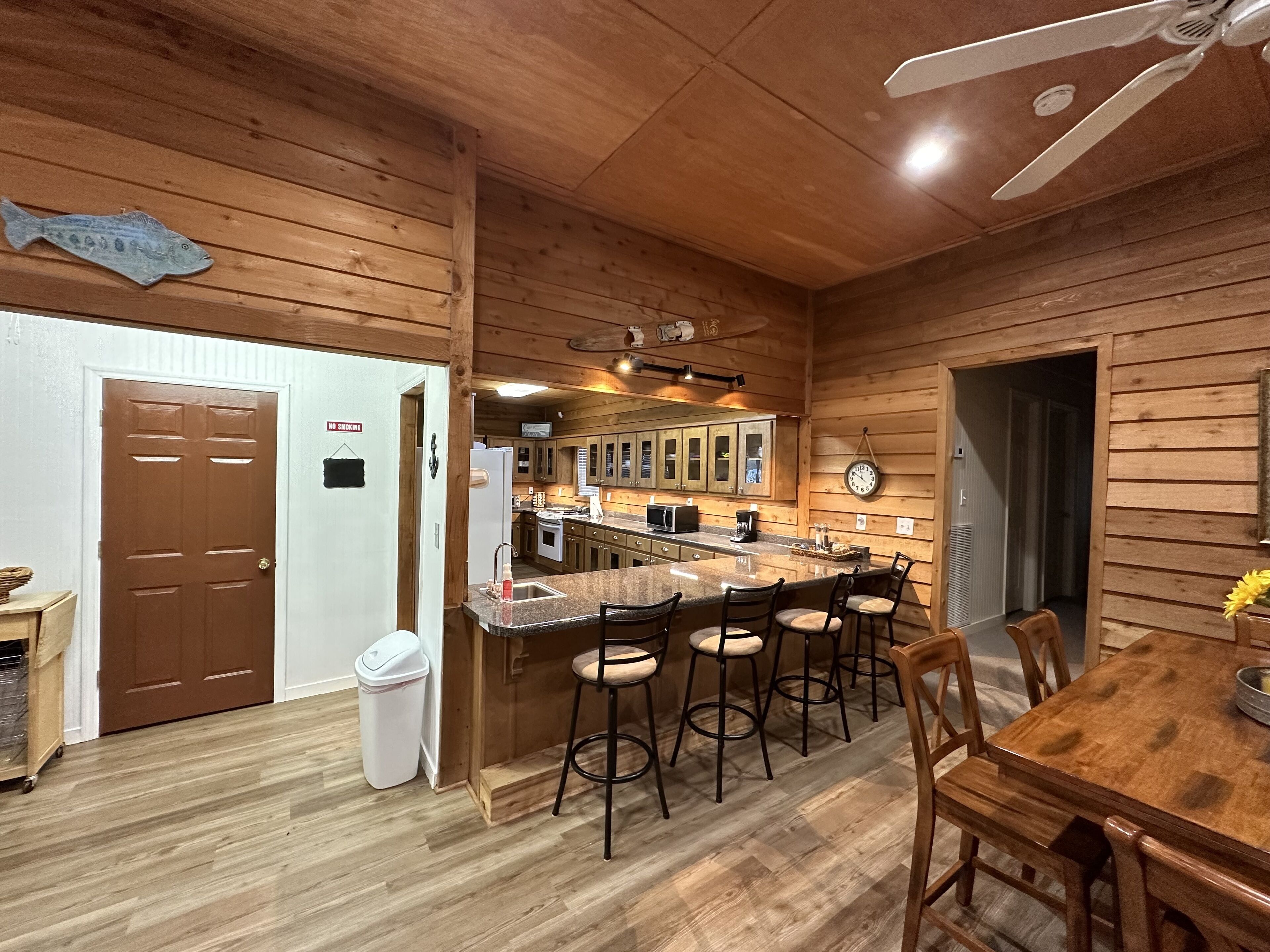 A wooden interior with a kitchen area, bar stools, and a dining table.