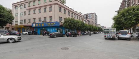 A street with buildings, parked cars, and a few pedestrians.
