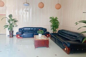 A living room with a black leather sofa, a wooden coffee table, and two potted plants. - Dongguan Xinyi Business Hotel (Xingtai Academy) (Dongguan)