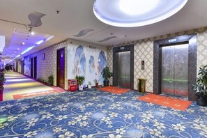 A hotel lobby with a patterned carpet, elevators, and potted plants. - Dongguan Xinyi Business Hotel (Xingtai Academy) (Dongguan)