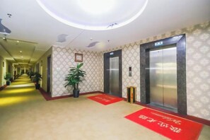 A hotel corridor with elevators, a red carpet, and a potted plant. - Dongguan Xinyi Business Hotel (Xingtai Academy) (Dongguan)