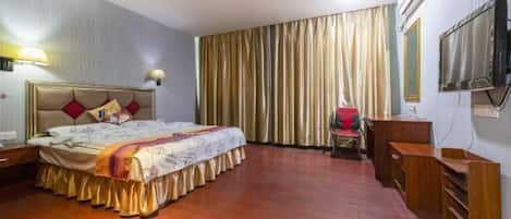 Habitación de hotel con cama, escritorio, silla, televisor y un ventanal con cortinas.