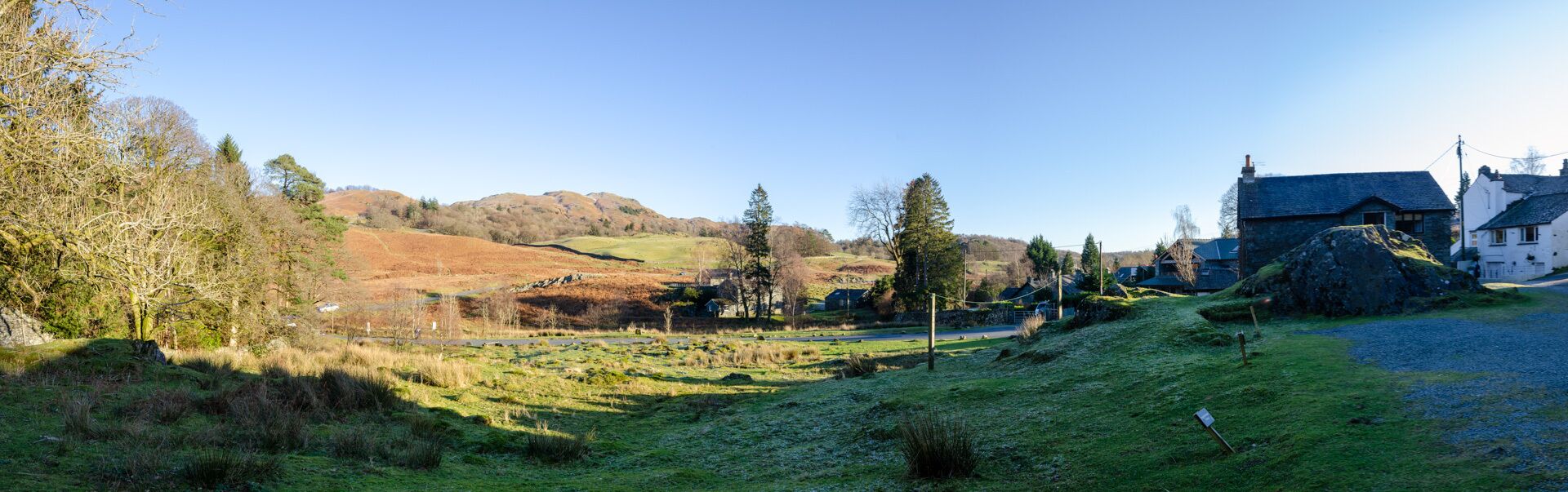 A rural landscape with a stone house, a grassy field, and a hill in the background.