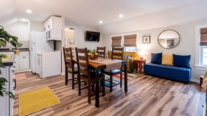 A modern kitchen with white appliances, a dining area with wooden chairs, a blue sofa, and a TV mounted on the wall. - The Back Yard-Upper Near Downtown LG |Balcony |Yard Now Dog Friendly (Lake Geneva)