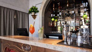 A bar area with a counter, two drinks, a cocktail shaker, and a wine rack in the background. - Pousada Alfama (Lisbon)