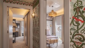 A hallway with patterned wallpaper, a bed with a white headboard, and a hanging light fixture. - Pousada Alfama (Lisbon)