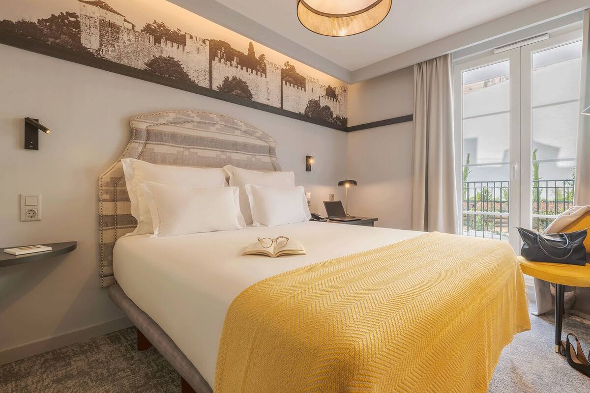 Une chambre d’hôtel avec un grand lit, une table de chevet, une chaise, un bureau avec une lampe et une vue sur l’extérieur.