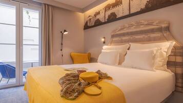 Habitación de hotel con una cama grande, cabecera amarilla y vista a un edificio a través de la ventana.