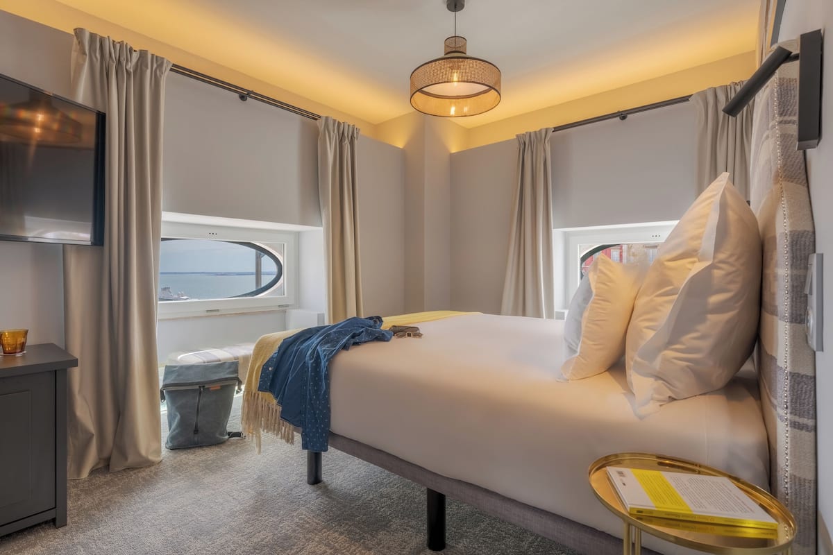 Une chambre d’hôtel avec un lit, une table de chevet, une télévision et une fenêtre avec des rideaux.