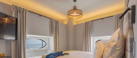 Quarto de hotel com uma cama, mesa de cabeceira, televisão e janela com cortinas.