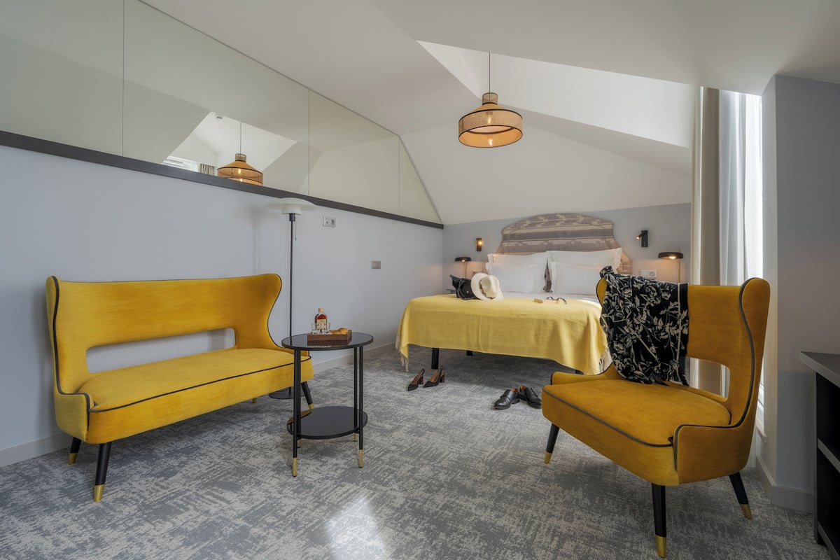 Une chambre moderne avec un lit, deux fauteuils jaunes, une petite table et une grande fenêtre.