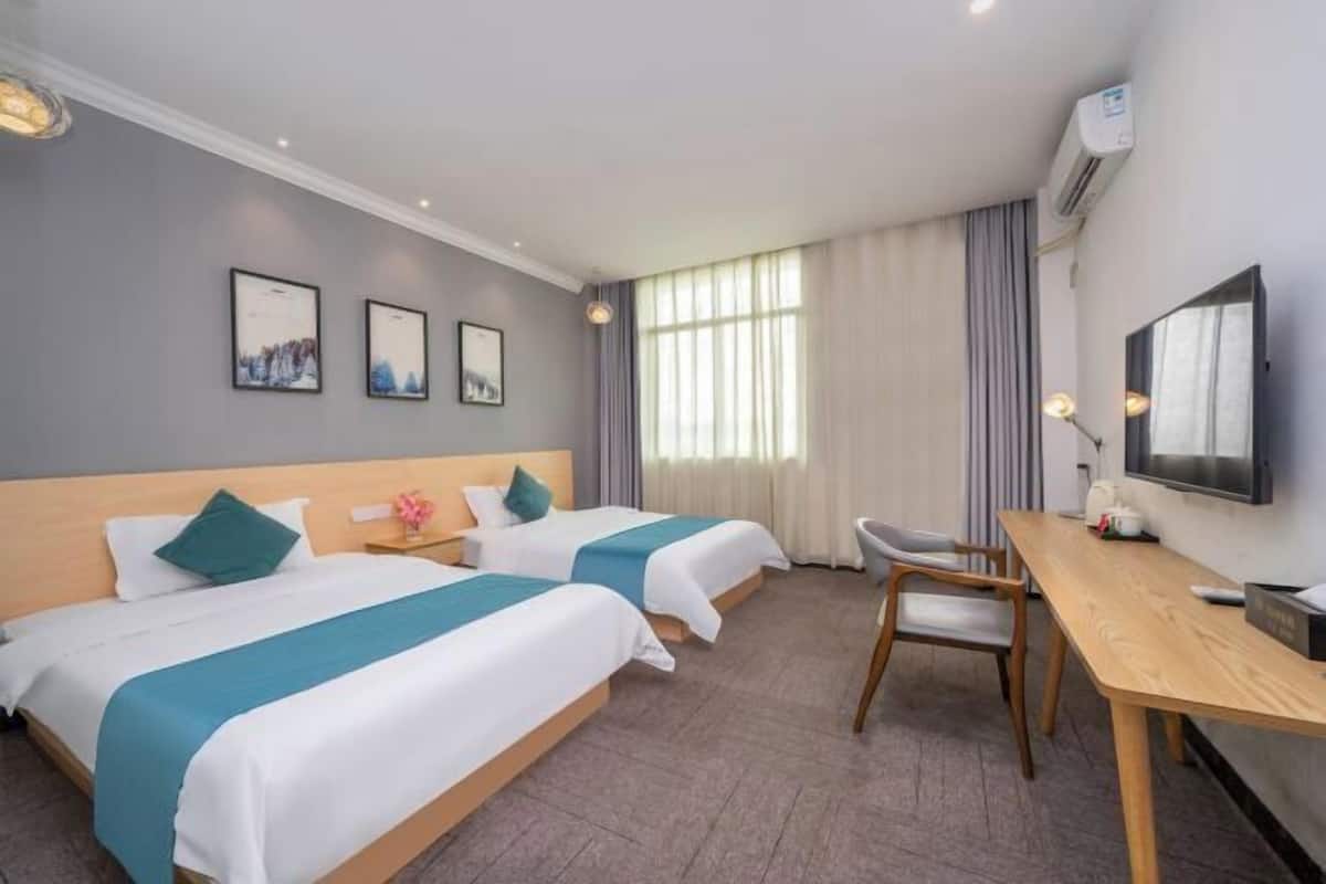 A hotel room with two beds, a desk, a chair, a TV, and framed pictures on the wall.