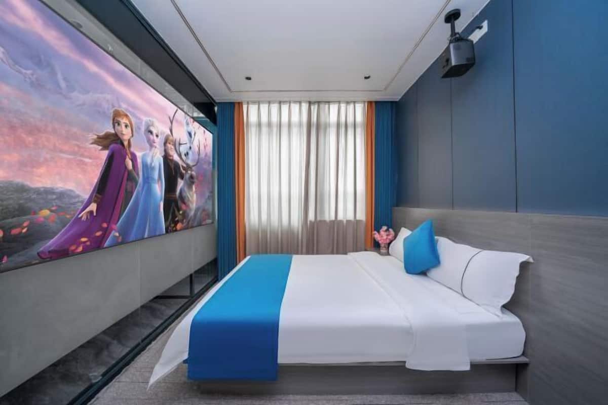 A hotel room with a large bed, a nightstand, a wall-mounted lamp, and a large window with curtains.