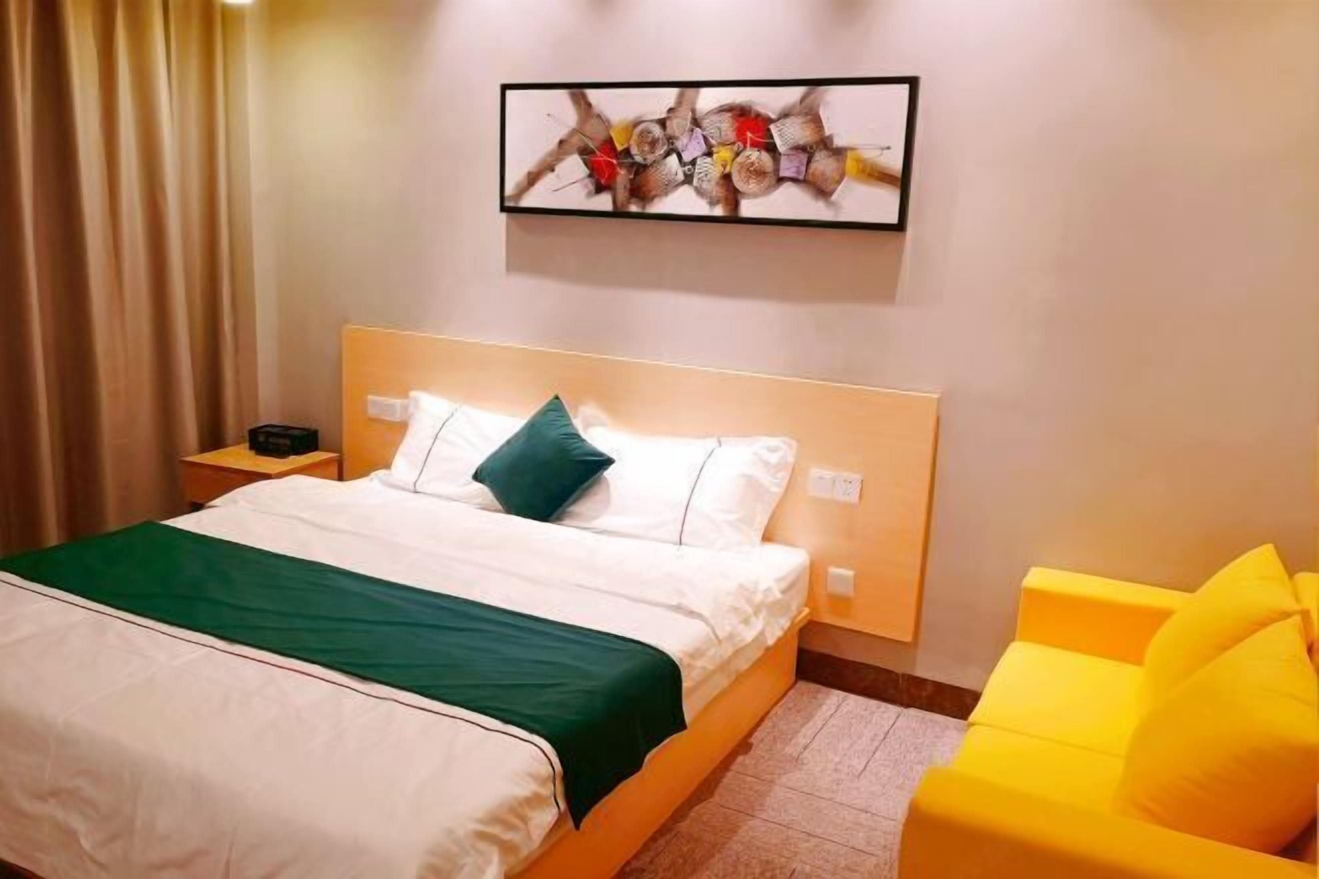 Een hotelkamer met een bed, een nachtkastje, een aan de muur hangend kunstwerk en een gele fauteuil.