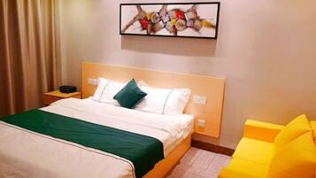 Een hotelkamer met een bed, een nachtkastje, een aan de muur hangend kunstwerk en een gele fauteuil.