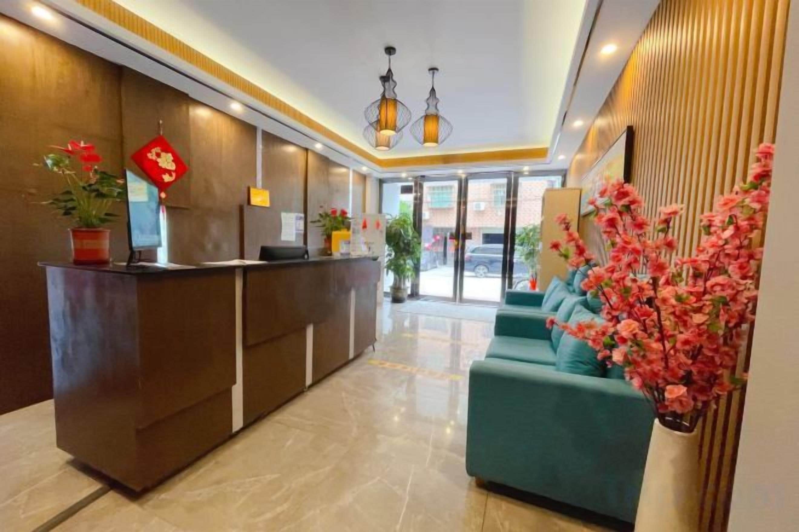 A hotel reception area with a reception desk, seating area, and potted plants.
