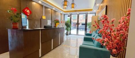 A hotel reception area with a reception desk, seating area, and potted plants.