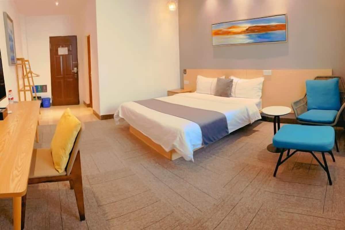 A hotel room with a bed, a desk, a chair, a small round table, and a painting on the wall.