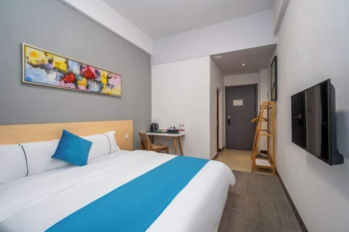 A hotel room with a bed, a desk, a chair, a TV, and a painting on the wall.