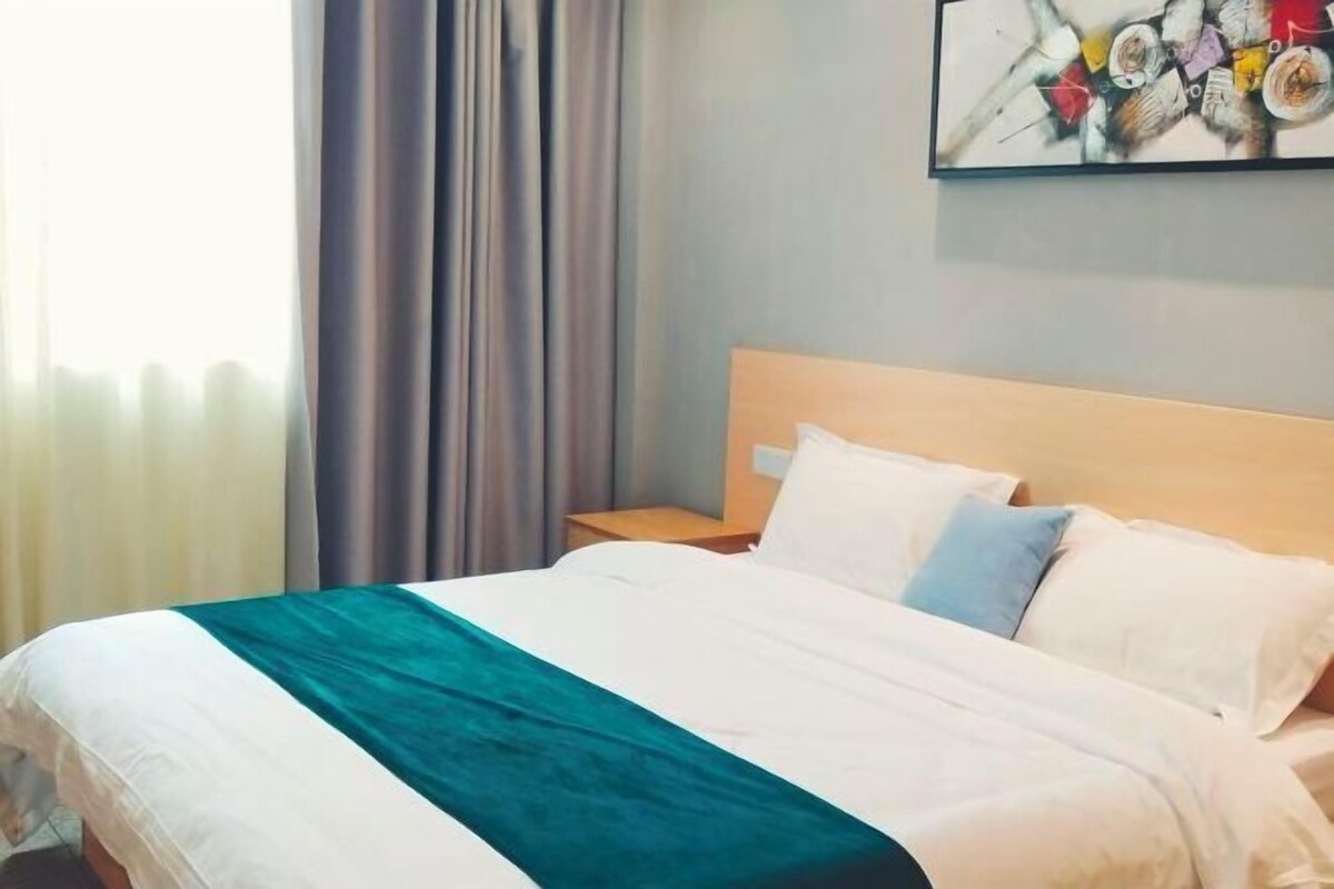 A hotel room with a bed, a nightstand, a painting on the wall, and a window with curtains.