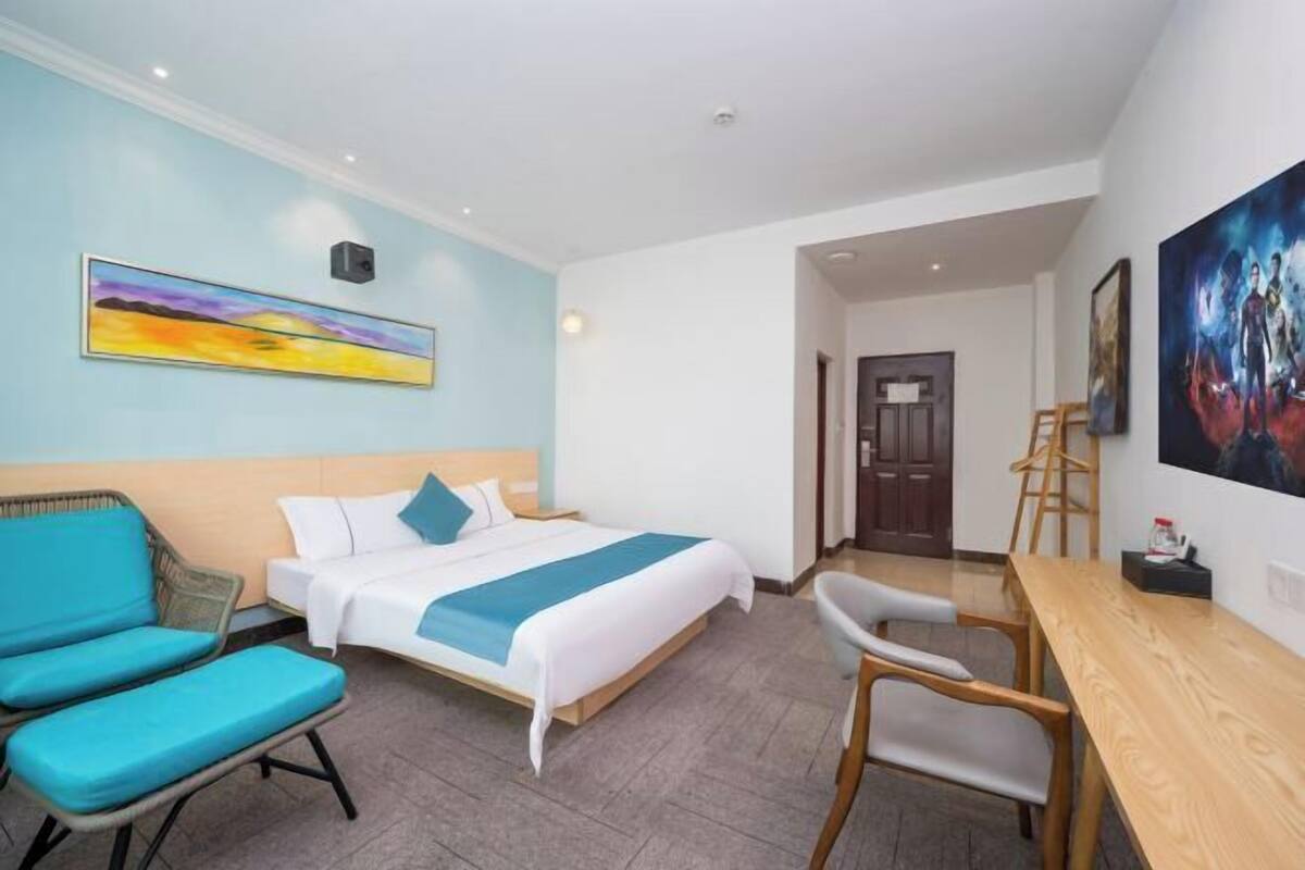 A hotel room with a bed, a desk, a chair, and a painting on the wall.