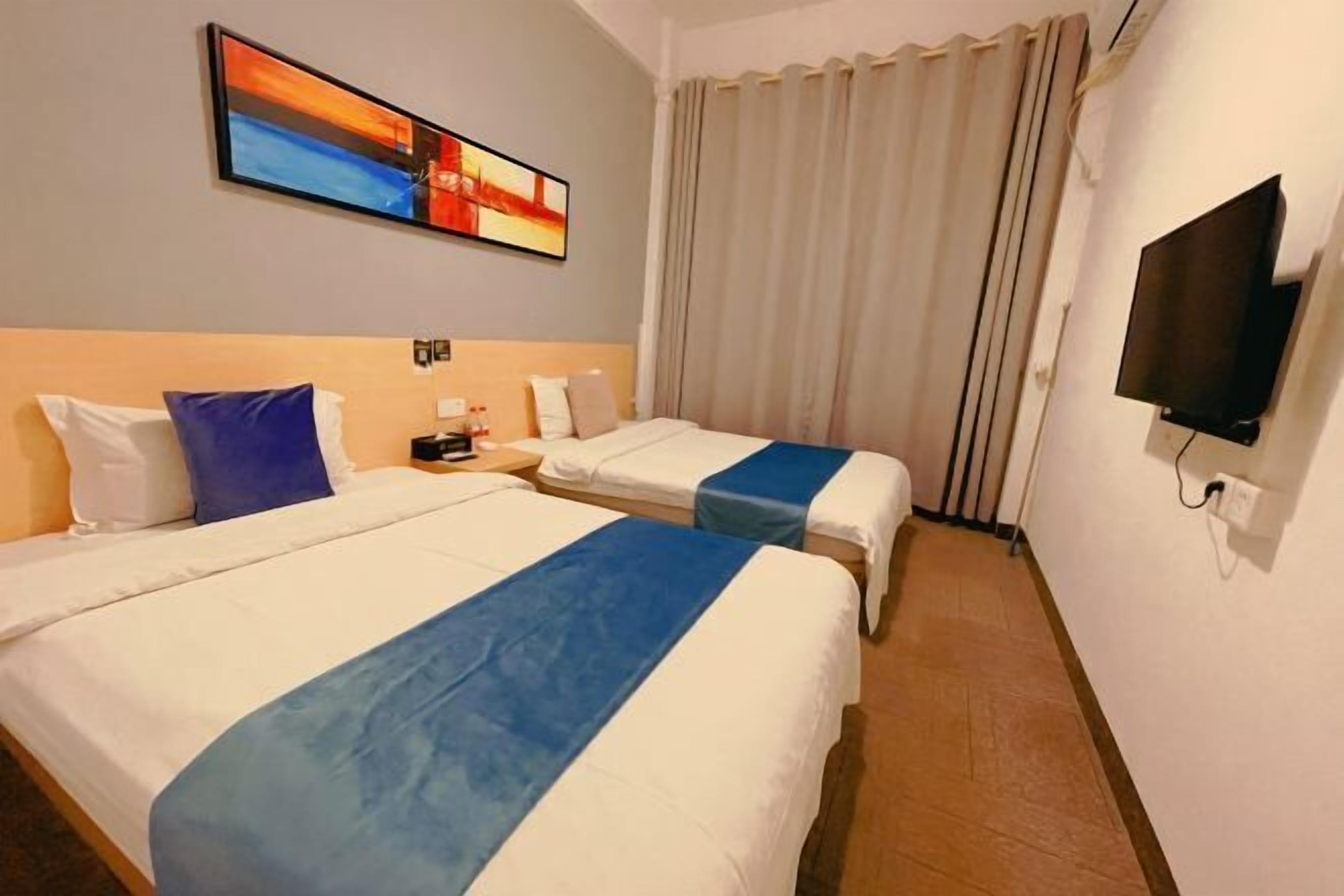 Een hotelkamer met twee bedden, een televisie en een schilderij aan de muur.