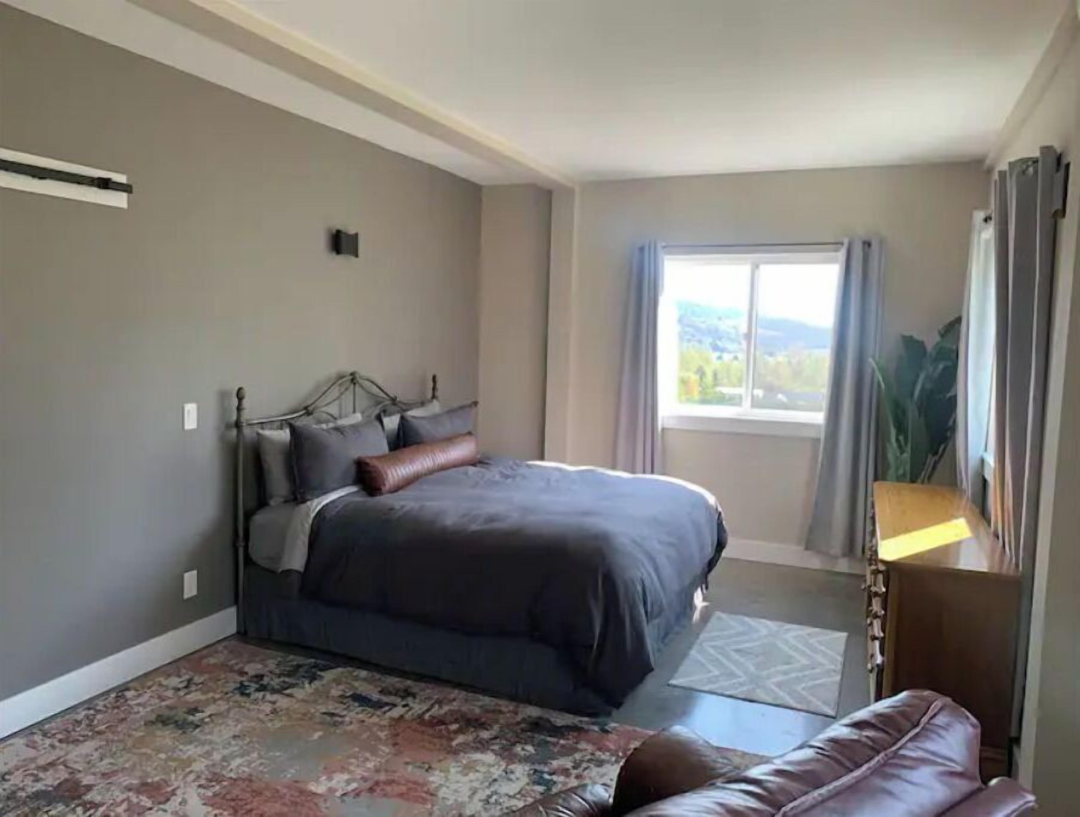 Een slaapkamer met een bed, een nachtkastje, een raam met gordijnen en uitzicht op de omgeving.