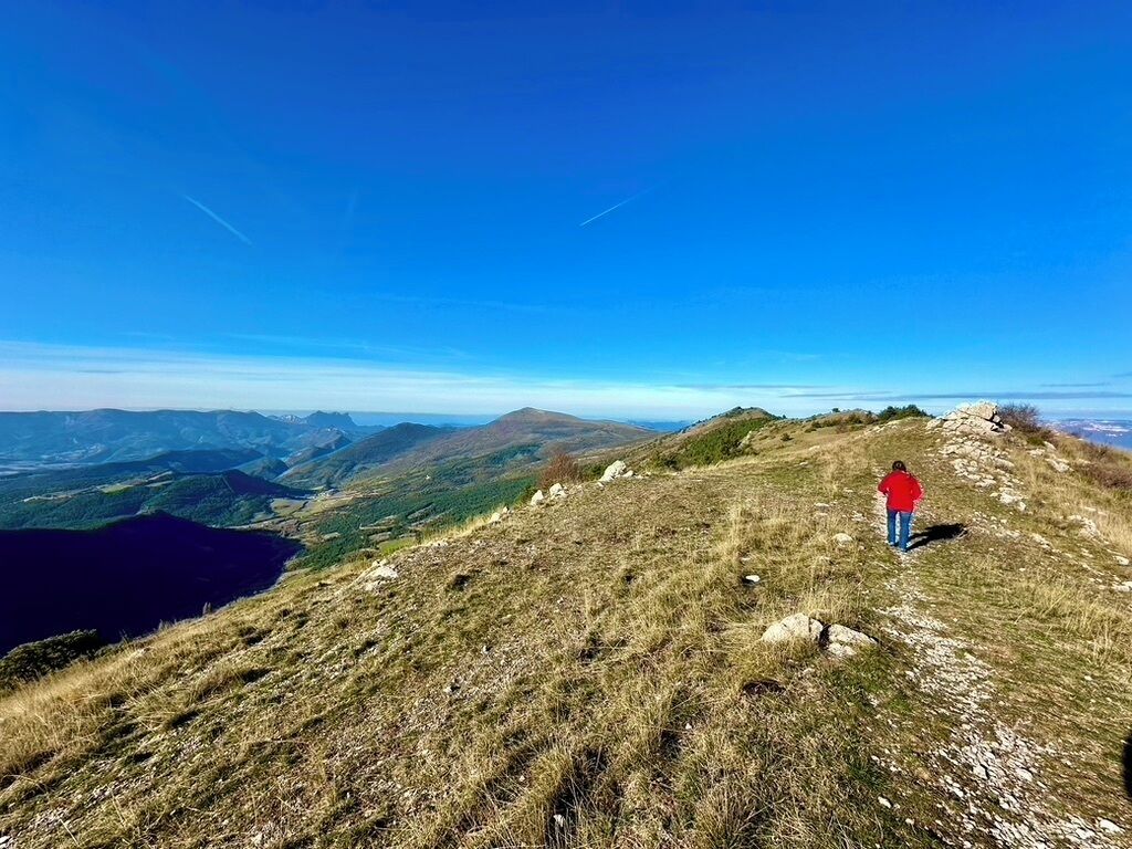 A person hiking on a grassy hill with a lake and mountains in the background.