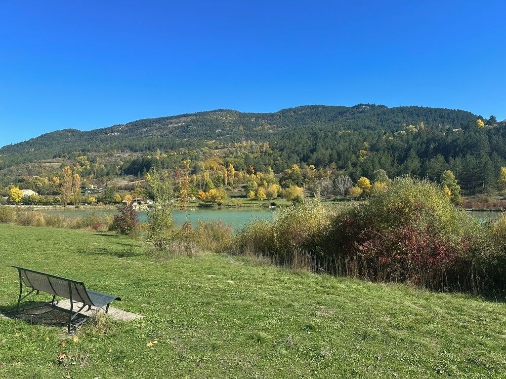 A grassy field with a bench, a lake, and hills in the background.