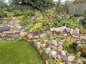 A garden with a stone wall, various plants, and a wooden fence.