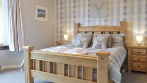 A wooden bed with a plaid headboard, two bedside tables, and a window with curtains. - 3 bedroom accommodation in Biggar (Biggar)