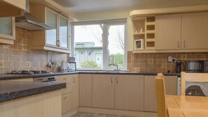 A modern kitchen with wooden cabinets, a gas stove, a microwave, and a built-in washing machine. - 3 bedroom accommodation in Biggar (Biggar)