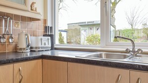 A kitchen with wooden cabinets, a stainless steel sink, a toaster, and a window with a view of a house and trees. - 3 bedroom accommodation in Biggar (Biggar)