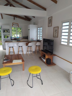 Une cuisine moderne avec des meubles blancs, un îlot central en bois et un coin repas agrémenté de tabourets jaunes.