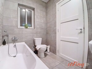 A modern bathroom with a bathtub, toilet, and a window above the toilet. - St Paul's  3BR Apartment - Spectacular Sea Views (San Pawl il-Bahar)