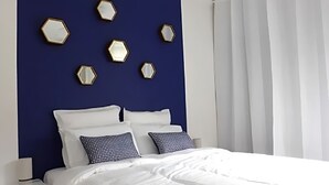 A bedroom with a dark blue wall, white bedding, and hexagonal mirrors on the wall. - Apartment center Cannes (Cannes)