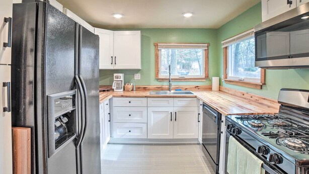Una cocina con armarios blancos, un refrigerador negro, encimera de madera, un lavamanos y una estufa.