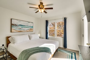 A bedroom with a bed, a ceiling fan, a window with curtains, and a painting on the wall.