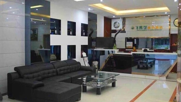 A modern lobby with a black sectional sofa, a glass coffee table, and a reception desk with a clock and a sign.
