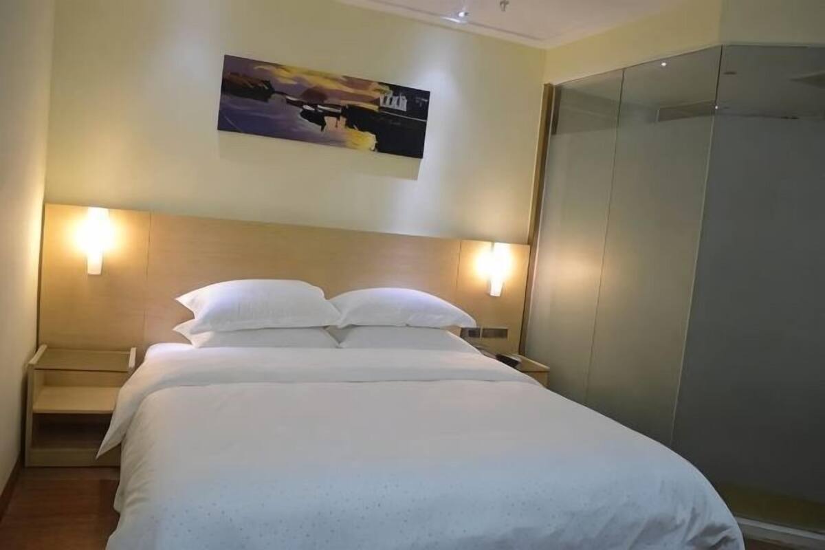 Une chambre d’hôtel avec un lit, deux lampes de chevet, une table de chevet, un tableau au mur et un dressing.