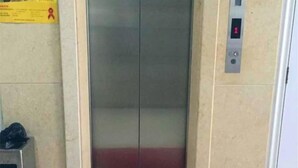 An elevator with a digital display showing the number 1, a control panel with buttons, and a yellow sign with red text on the wall.