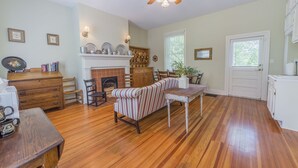 A spacious living room with hardwood floors, a fireplace, a dining area with a striped sofa, and a ceiling fan.