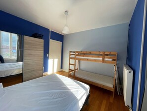 Quarto com cama beliche, janela ampla e radiador.